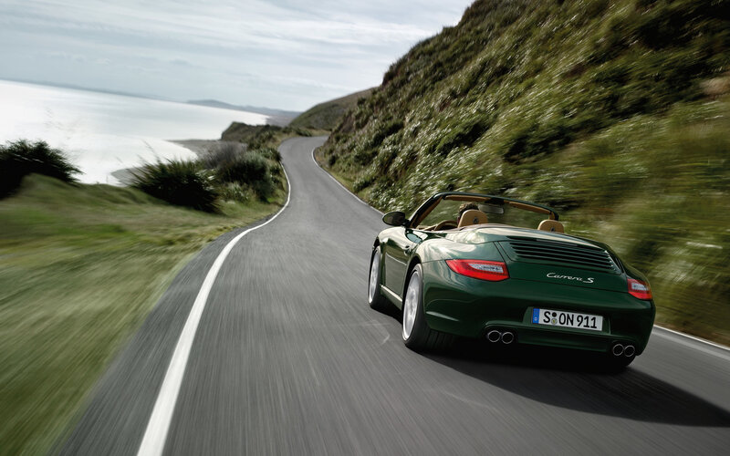Green Porsche driving on coastal road