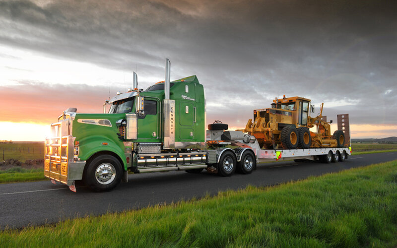 Green truck hauling construction equipment