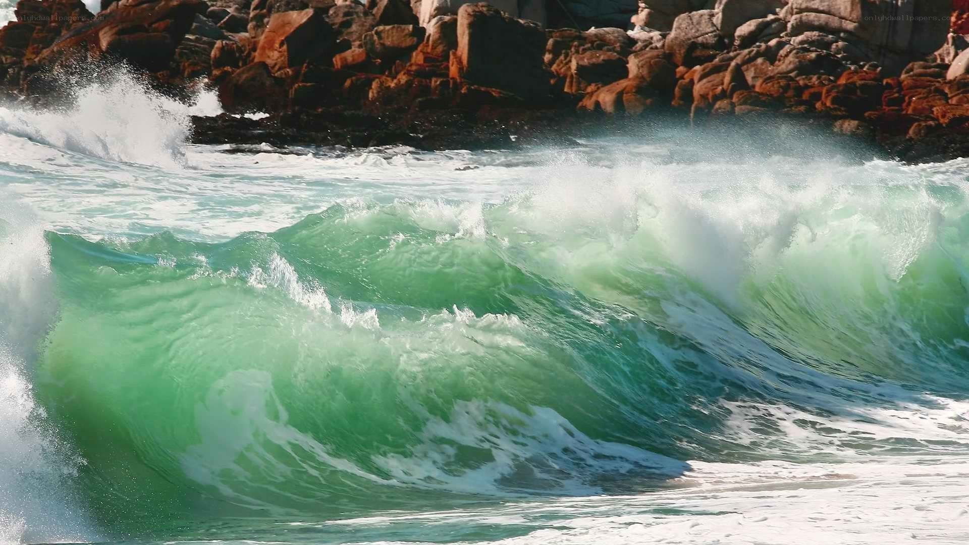 Green wave crashing on rocks