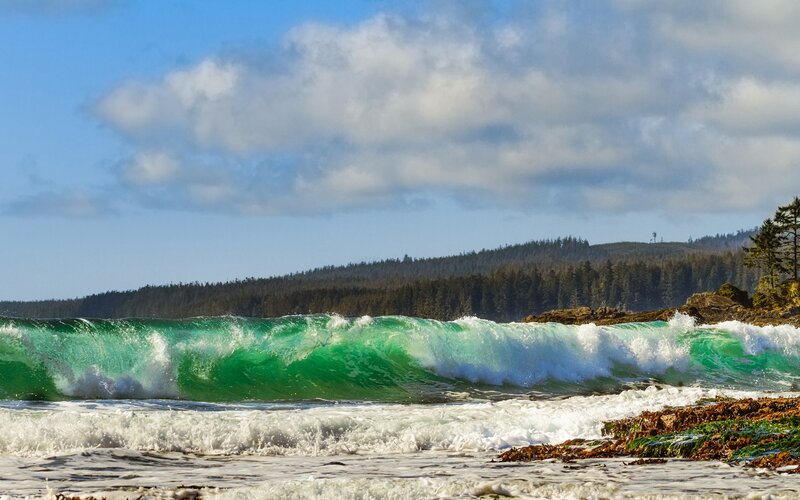 Green wave crashing on rocky shore
