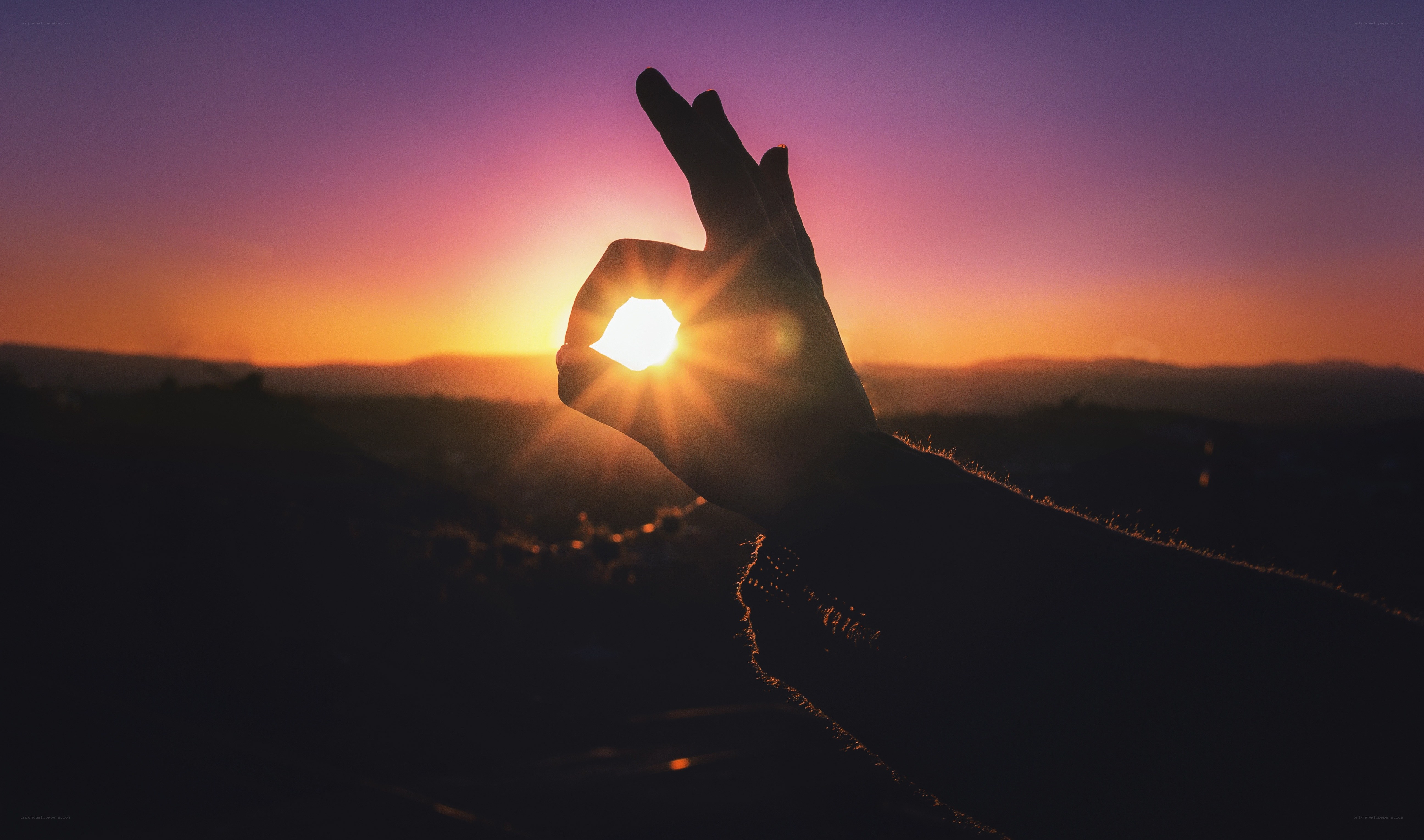 hand framing the setting sun
