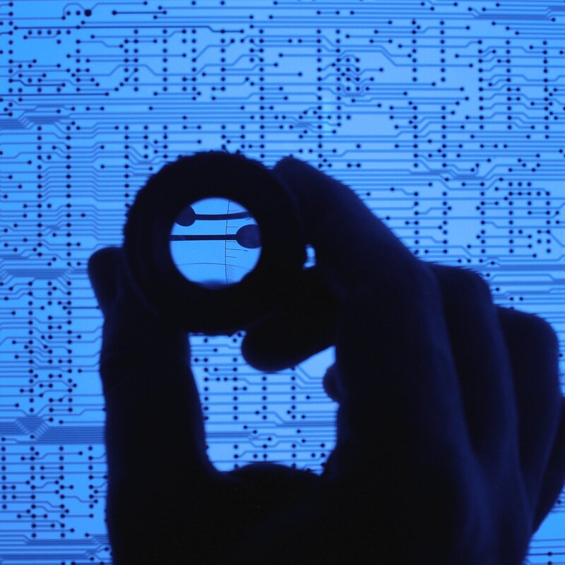 Hand holding magnifying glass over circuit board