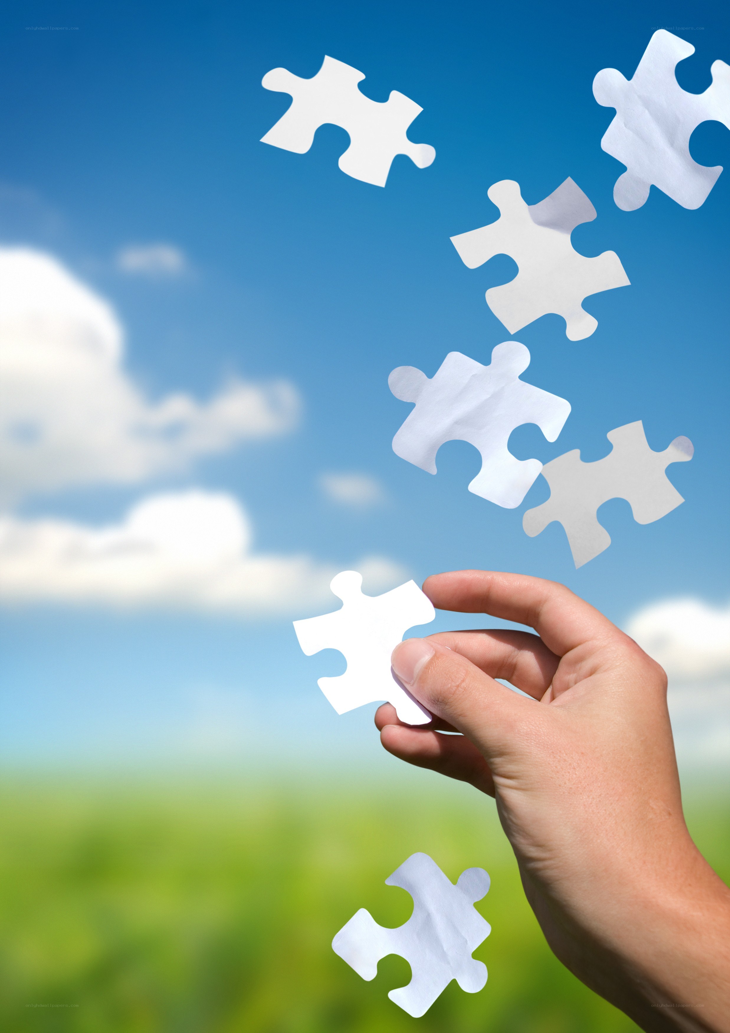 Hand holding puzzle piece against sky