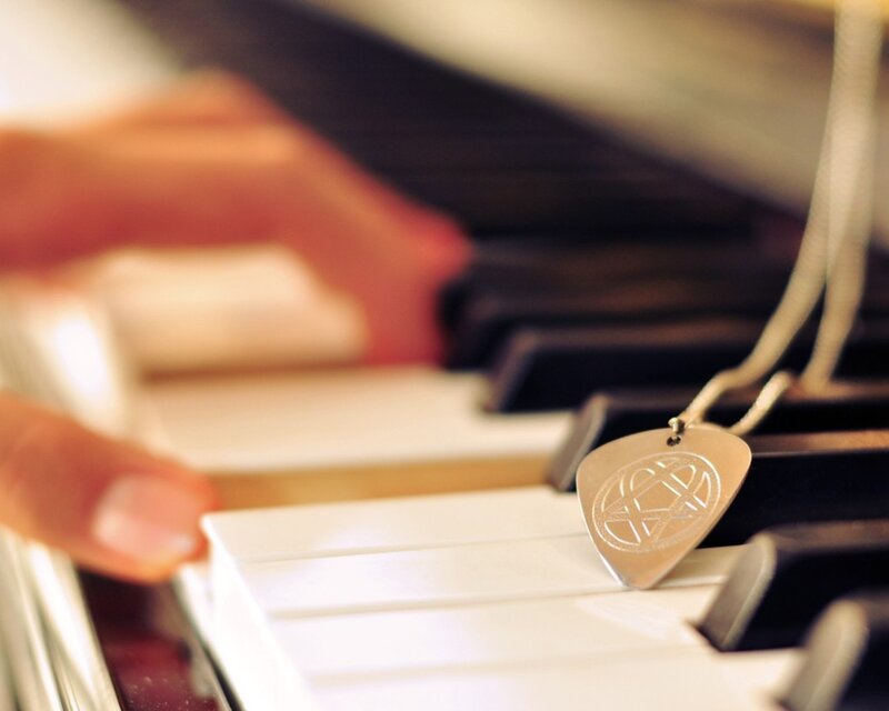 hand on piano keys with guitar pick pendant