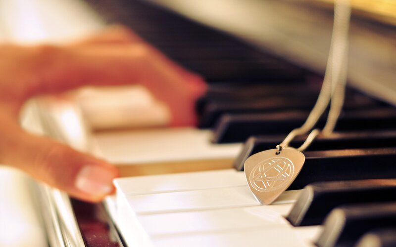 hand on piano keys with guitar pick