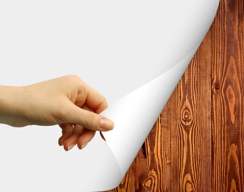 hand peeling paper to reveal wood