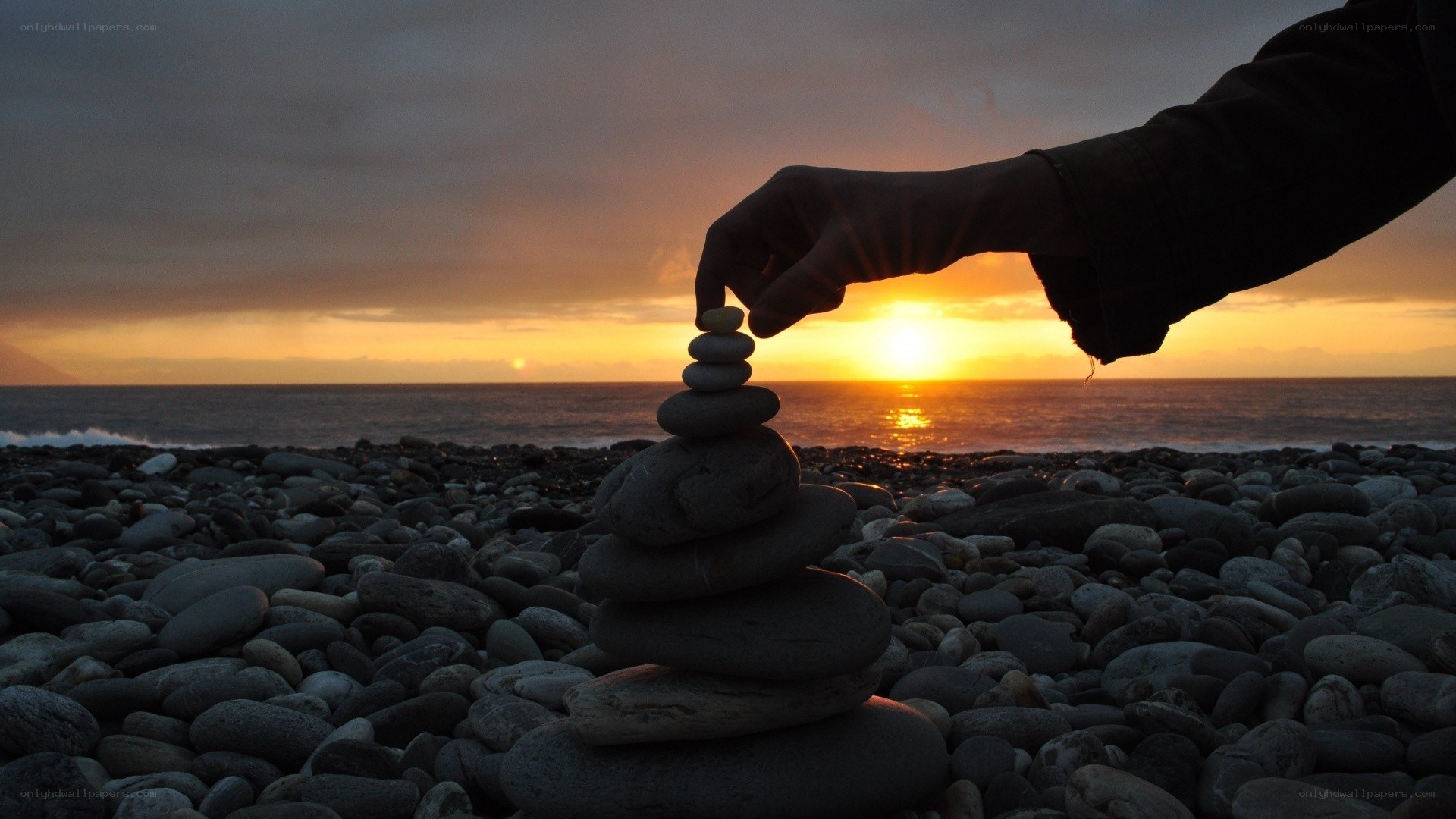 hand stacking stones at sunset