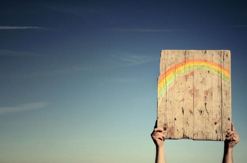 hands holding wooden rainbow sign