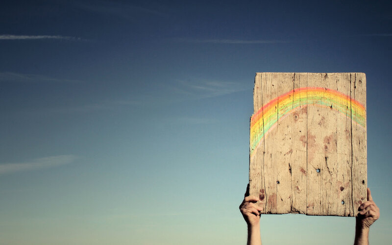 Hands holding wooden sign with rainbow
