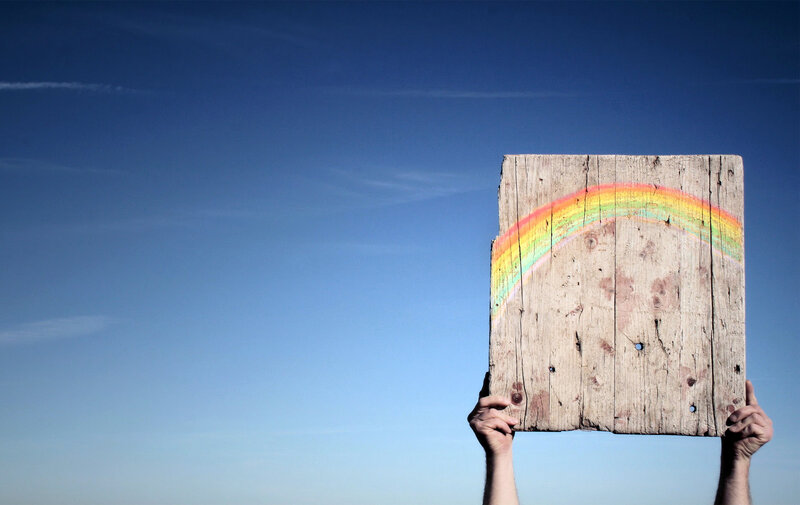 hands holding wooden sign with rainbow