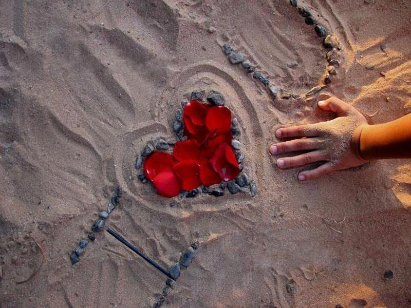 heart drawn in sand with rose petals