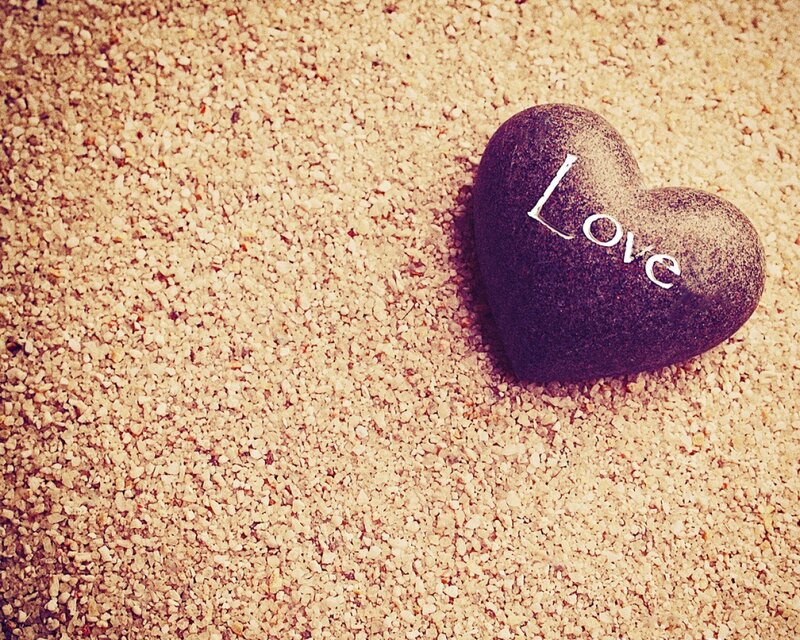 Heart-shaped stone with 'Love' on sand