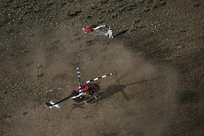 Helicopter and parachutist on desert terrain