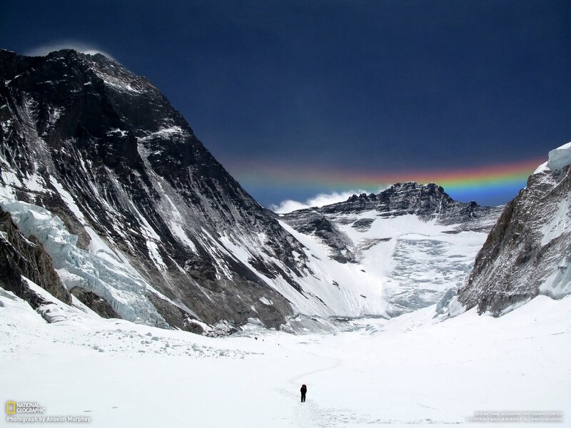 Hiker on snowy mountain with rainbow