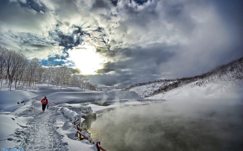 Hiker on snowy path near steaming river