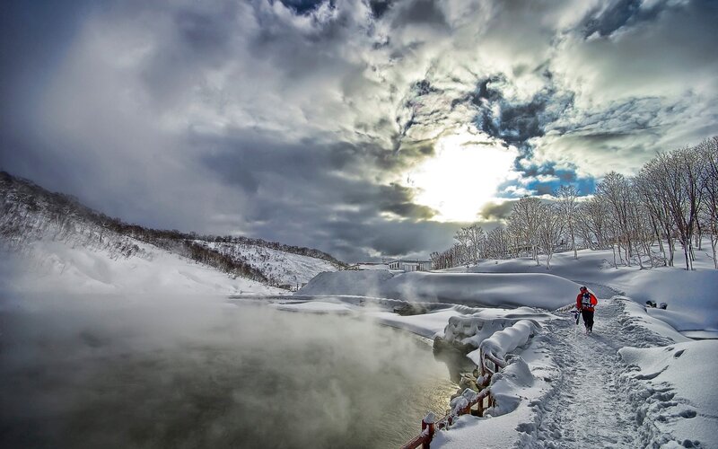 Hiker on snowy path near steaming river