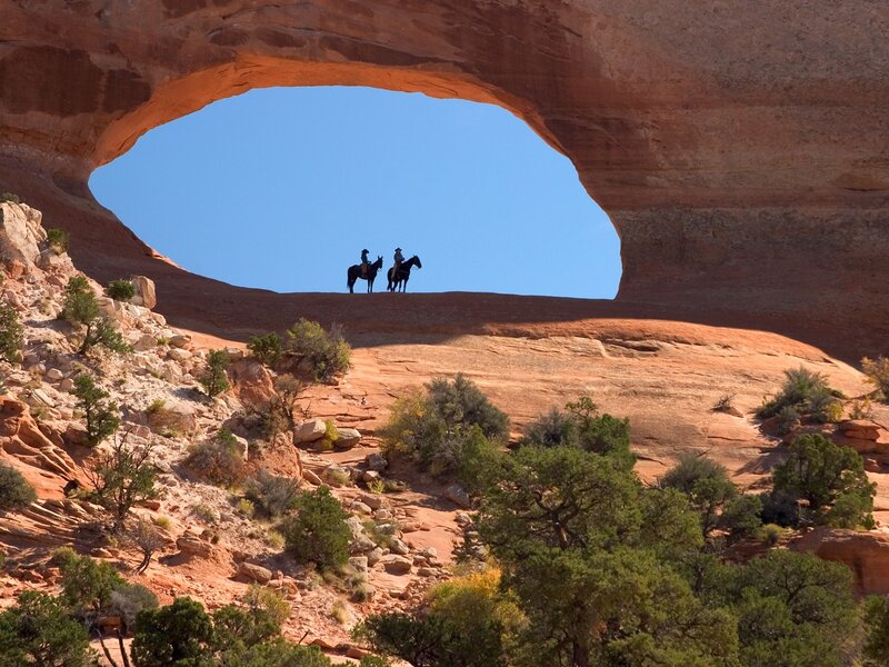 Horseback riders under a natural arch