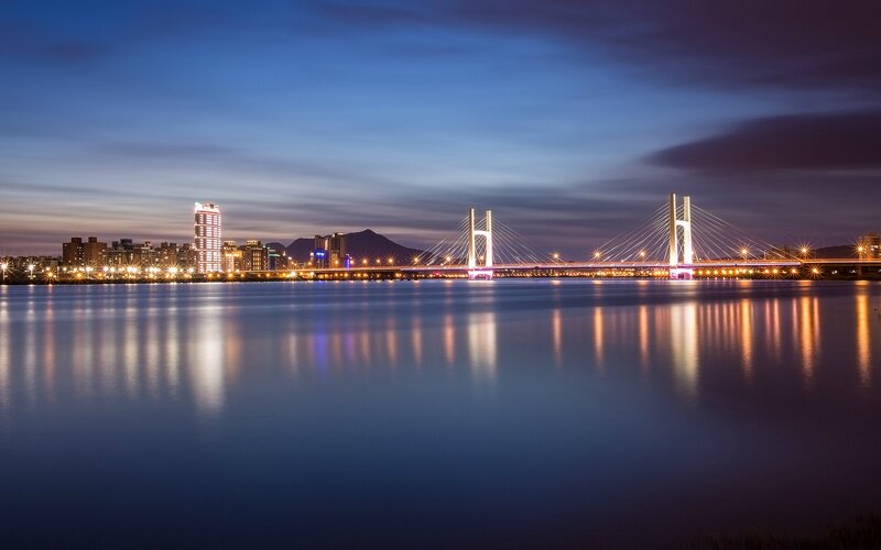 Illuminated Cable-stayed Bridge — Blue, Serene, Night, Photograph, City Skyline, River, Mountain