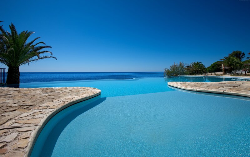 Infinity Pool Overlooking Ocean — Blue, Serene, Afternoon, Photograph, Palm Tree, Stone Deck