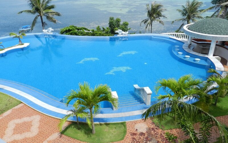 Infinity Pool Overlooking Ocean — Blue, Serene, Afternoon, Photograph, Palm Trees, Statues