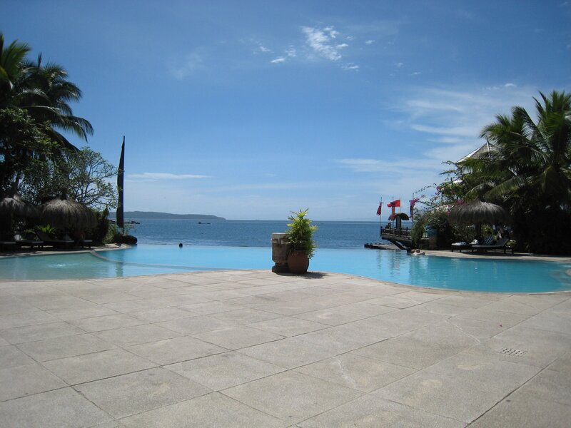 Infinity Pool Overlooking Ocean — Blue, Serene, Afternoon, Photograph, Palm Trees, Thatched Umbrellas