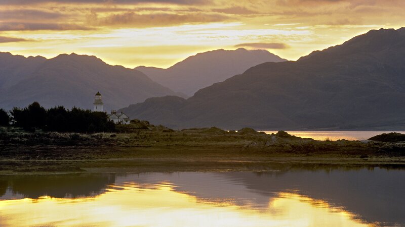 Lighthouse at sunset by mountains