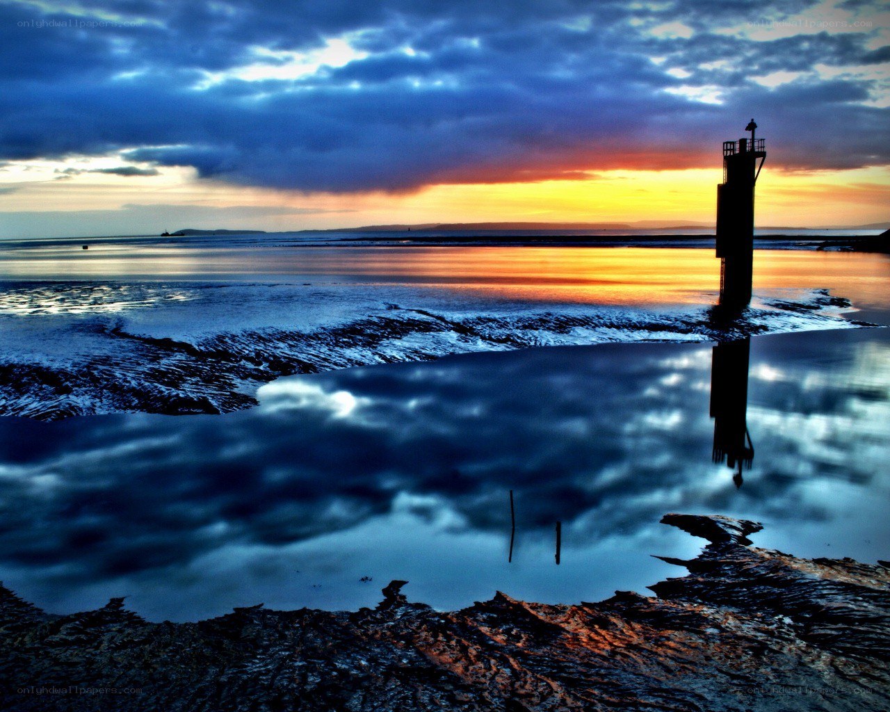 Lighthouse at sunset on a reflective shore