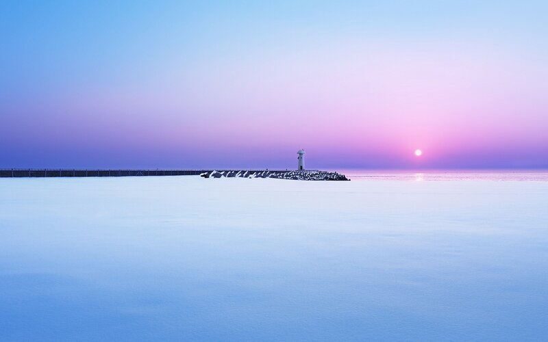 Lighthouse at sunset over frozen sea