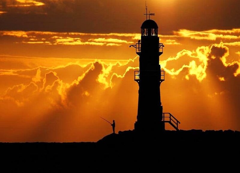 Lighthouse at sunset with fisherman