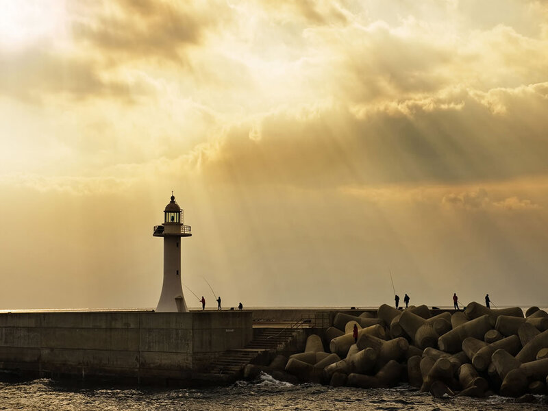 Lighthouse at sunset with fishing silhouettes