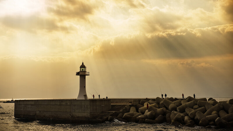 Lighthouse at sunset with fishing silhouettes