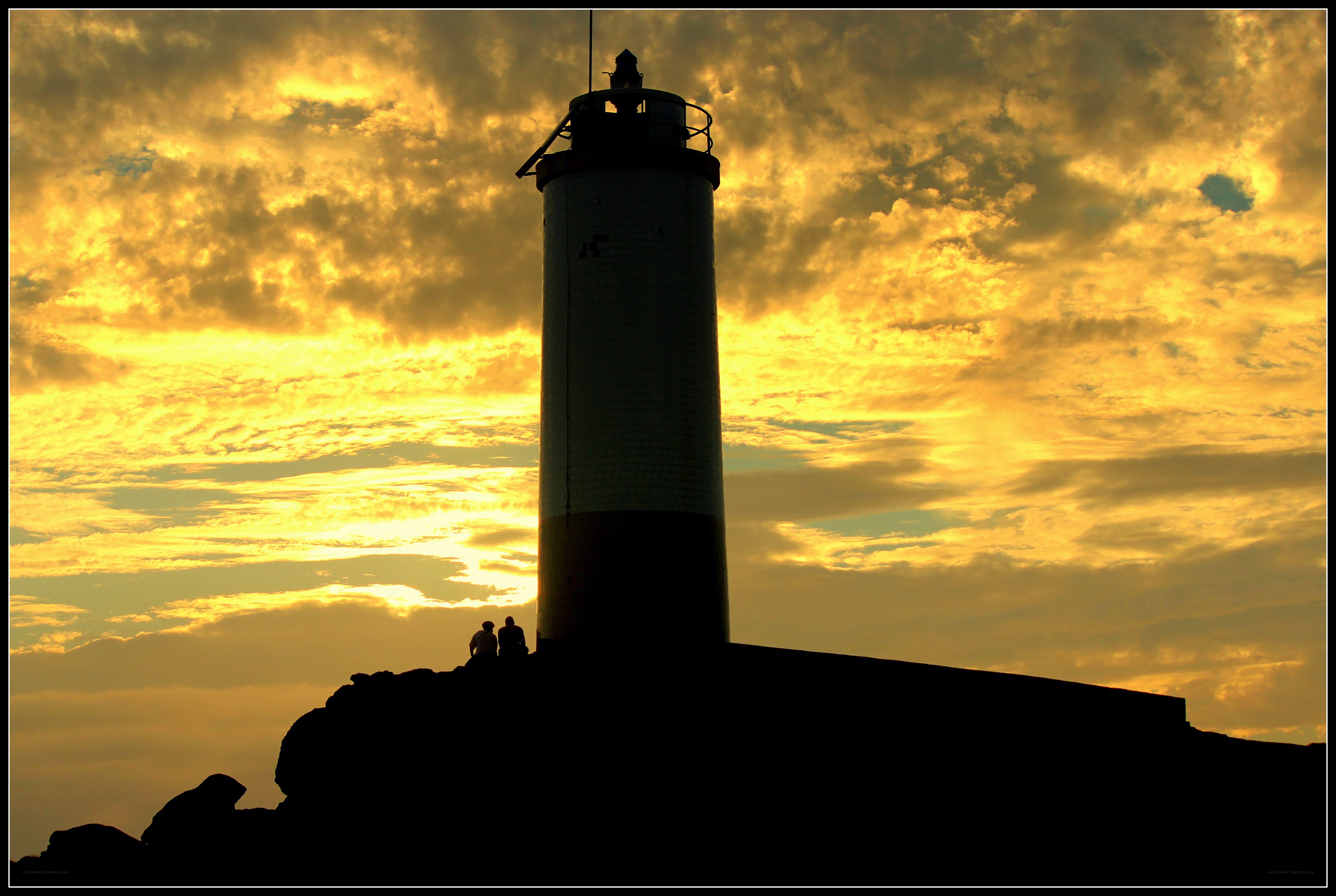 Lighthouse at sunset with silhouetted figures