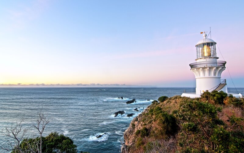 Lighthouse on Coastal Cliff — Blue, Serene, Sunset, Photograph, Ocean, Sky, Rocks, White