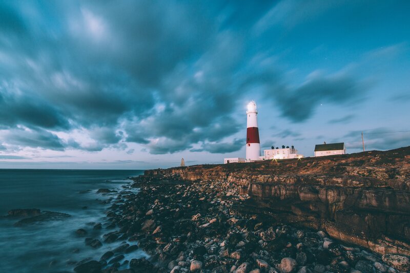 Lighthouse on Rocky Cliff — Blue, Dramatic, Sunset, Photograph, Ocean, Clouds, Rocks