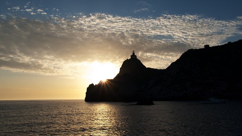 Lighthouse on Rocky Cliff — Blue, Dramatic, Sunset, Photograph, Sun