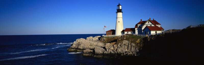 Lighthouse on Rocky Cliff — Blue, Serene, Afternoon, Photograph, Ocean, Sky, Flag