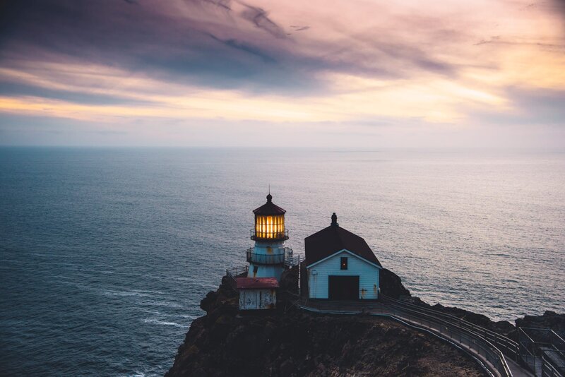 Lighthouse on Rocky Cliff — Blue, Serene, Sunset, Photograph, Ocean, Sky, Building