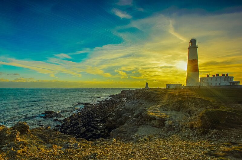 Lighthouse on Rocky Coast — Blue, Dramatic, Sunset, Photograph, Ocean, Sky, Rocks