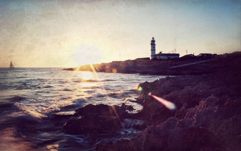 Lighthouse on Rocky Coast — Blue, Serene, Sunset, Photograph, Sailboat