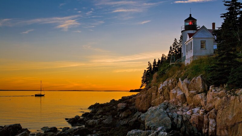 Lighthouse on Rocky Coast — Orange, Serene, Sunset, Photograph, Sailboat, Rocks