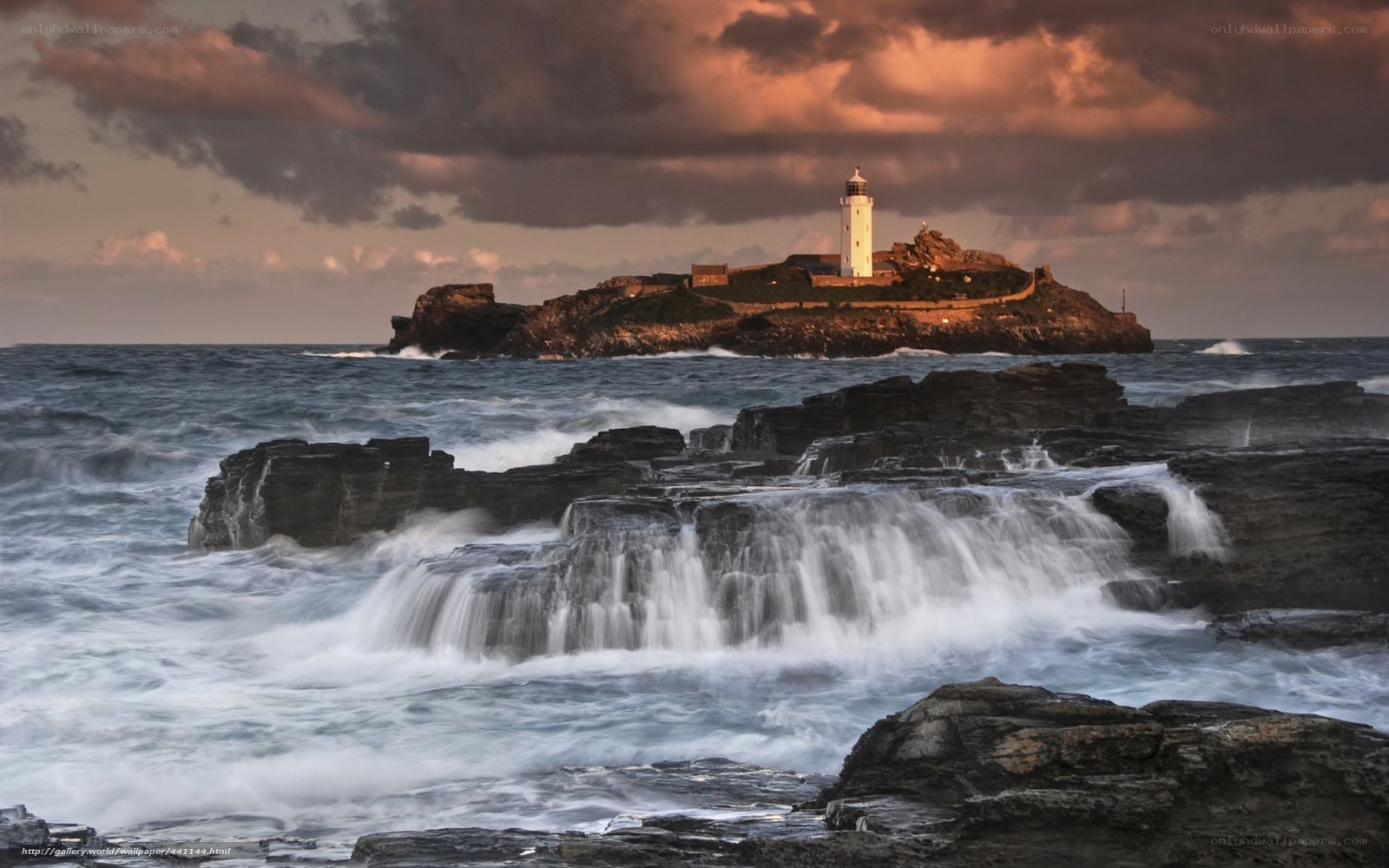 Lighthouse on rocky island at sunset