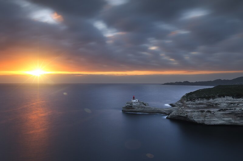 Lighthouse on Rocky Island — Orange, Dramatic, Sunset, Photograph, Sun, Ocean, Cliffs