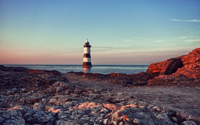 lighthouse on rocky shore at sunset