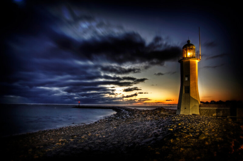 Lighthouse on Rocky Shore — Blue, Dramatic, Sunset, Photograph, Ocean, Sky, Clouds