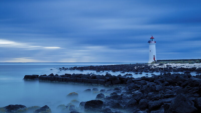 Lighthouse on Rocky Shore — Blue, Serene, Night, Photograph, Rocks, Sea