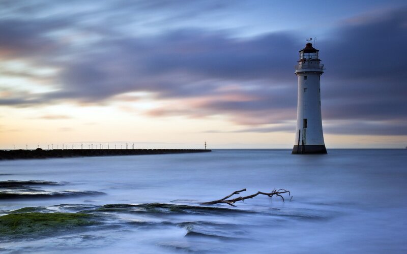 Lighthouse on Rocky Shore — Blue, Serene, Sunset, Photograph, Driftwood, Pier