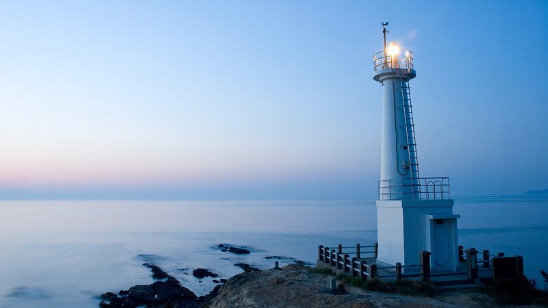 Lighthouse on Rocky Shore — Blue, Serene, Sunset, Photograph, Ocean, Sky, Rocks