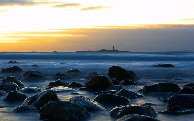 Lighthouse on Rocky Shore — Blue, Serene, Sunset, Photograph, Rocks, Ocean