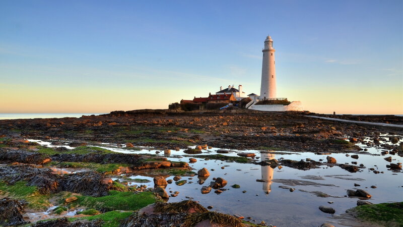 Lighthouse on Rocky Shore — Blue, Serene, Sunset, Photograph, Rocks, Sea, Sky, Reflection