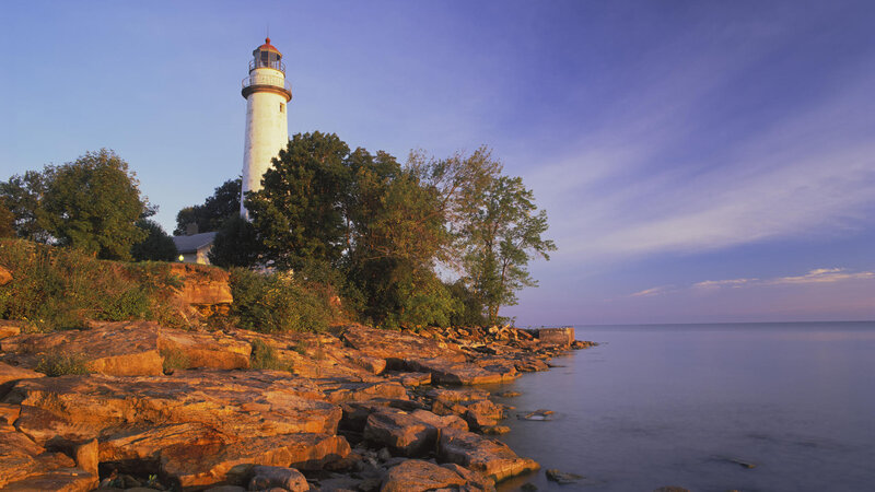 Lighthouse on Rocky Shore — Blue, Serene, Sunset, Photograph, Trees